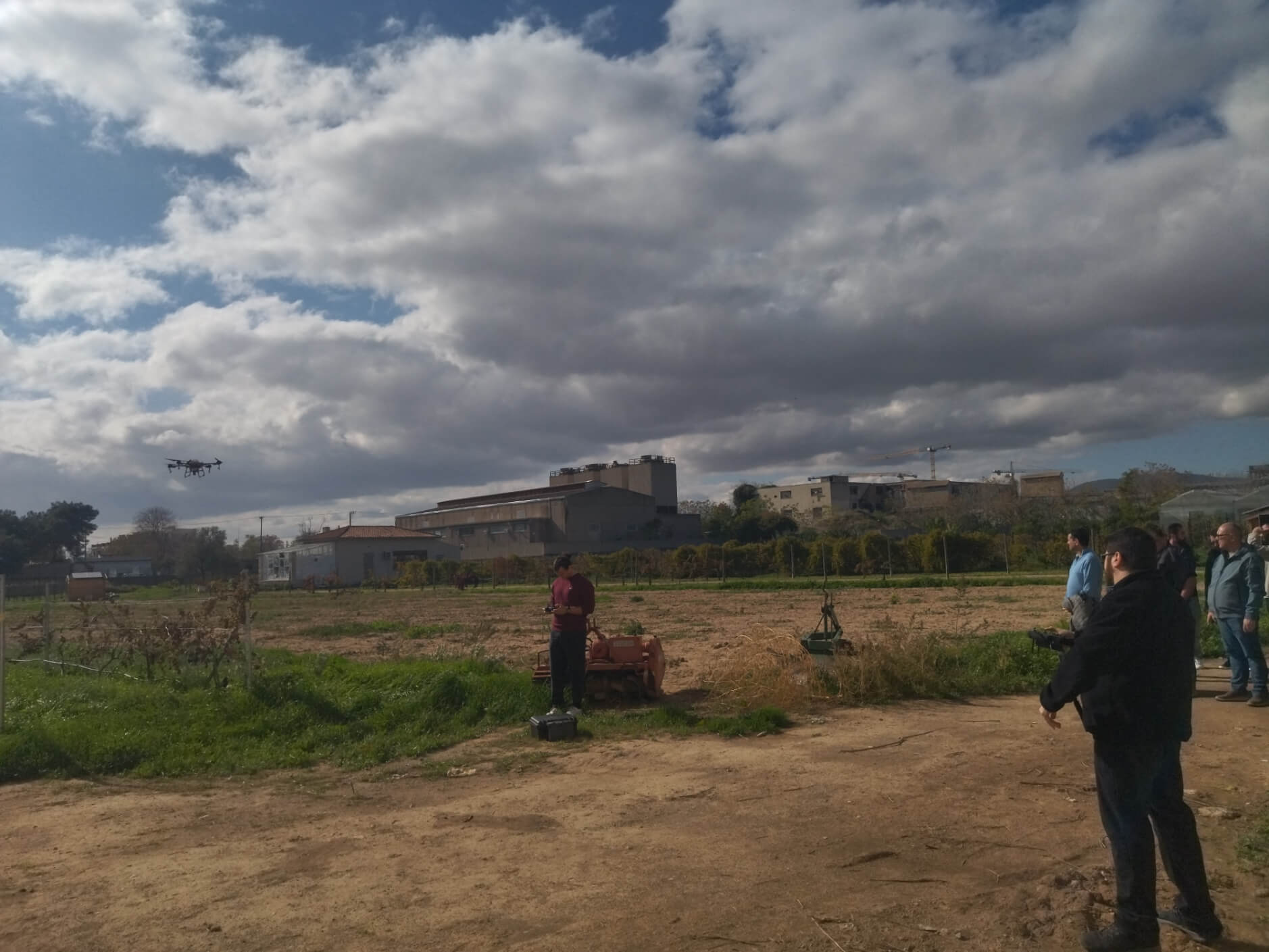 Spraying drone in flight over the field, attendees watching